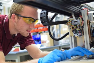 A student wearing yellow safety glasses and a maroon polo works in the DREAM machine.